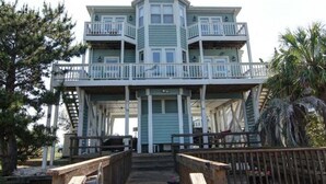 A multi-story building with a balcony, wooden deck, and a staircase leading to the upper levels. - Turtle Cove is a spacious 4-bed home in Holden Beach, perfect for 9 guests. (Holden Beach)