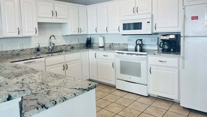 Cucina con mobili bianchi, piano di lavoro in granito, forno a microonde, fornello e frigorifero.