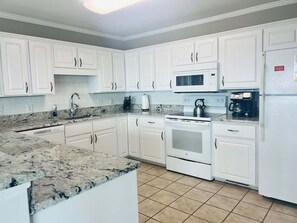 A kitchen with white cabinets, a granite countertop, a microwave, a stove, and a refrigerator.