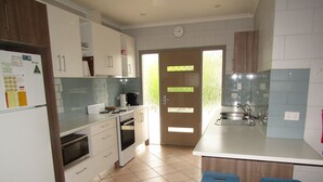 A modern kitchen with white cabinets, a built-in oven, a coffee maker, and a sink. There are two blue stools and a door leading to another room. - The Catch  ~ short walk to beach! Dog Friendly  - Off Peak Special! (Stansbury)