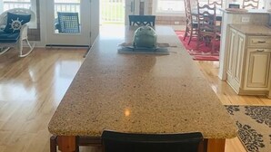 A kitchen with a granite countertop, wooden chairs, and a hanging light fixture. - Experience luxury at Shore Beats Workin', a spacious 5BR retreat in Holden Beach. (Holden Beach)