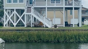 A multi-story waterfront building with balconies, a covered porch, and a staircase leading to the upper levels. - Experience luxury at Shore Beats Workin', a spacious 5BR retreat in Holden Beach. (Holden Beach)