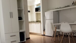 Eine moderne Küche mit weißen Schränken, einer Mikrowelle und einem Kühlschrank. Ein Essbereich mit weißen Stühlen und einem Tisch ist ebenfalls vorhanden.