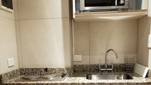 Eine Küche mit eingebauter Mikrowelle, Spüle aus Edelstahl, Arbeitsplatte aus Granit und hellen Holzschränken.