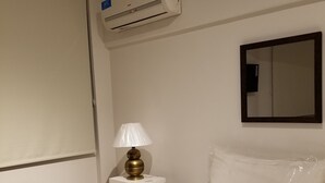Ein Hotelzimmer mit Bett, Nachttischlampe, Wand-Klimaanlage und Spiegel.