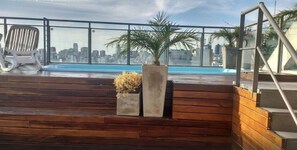 A rooftop terrace with a view of a city skyline, a pool, and wooden steps. - Studio Bulnes (Buenos Aires)