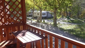Una terraza de madera con una mesa y sillas, con vista a un camping con vehículos recreativos y árboles.