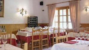 Un comedor con mesas y sillas de madera, manteles blancos y copas de vino preparadas para una comida.