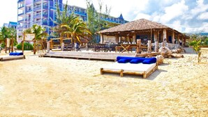 Un resort frente al mar con una cabaña de techo de paja, muelle de madera y sillas de descanso.