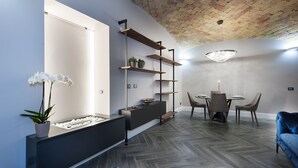 A modern living room with a herringbone wood floor, a dark sofa, a blue armchair, a dining area with a round table and chairs, and a brick ceiling. - Luma Suite Via Veneto - Roma . Your private luxury nest in Rome (Roma)