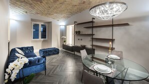 A modern living room with a blue sofa, a glass dining table, and a brick ceiling. - Luma Suite Via Veneto - Roma . Your private luxury nest in Rome (Roma)