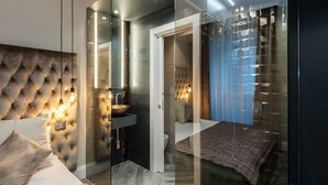 A modern bedroom with a tufted headboard, a glass-enclosed vanity, a bed with a textured blanket, and a geometric-patterned wall. - Luma Suite Via Veneto - Roma . Your private luxury nest in Rome (Roma)