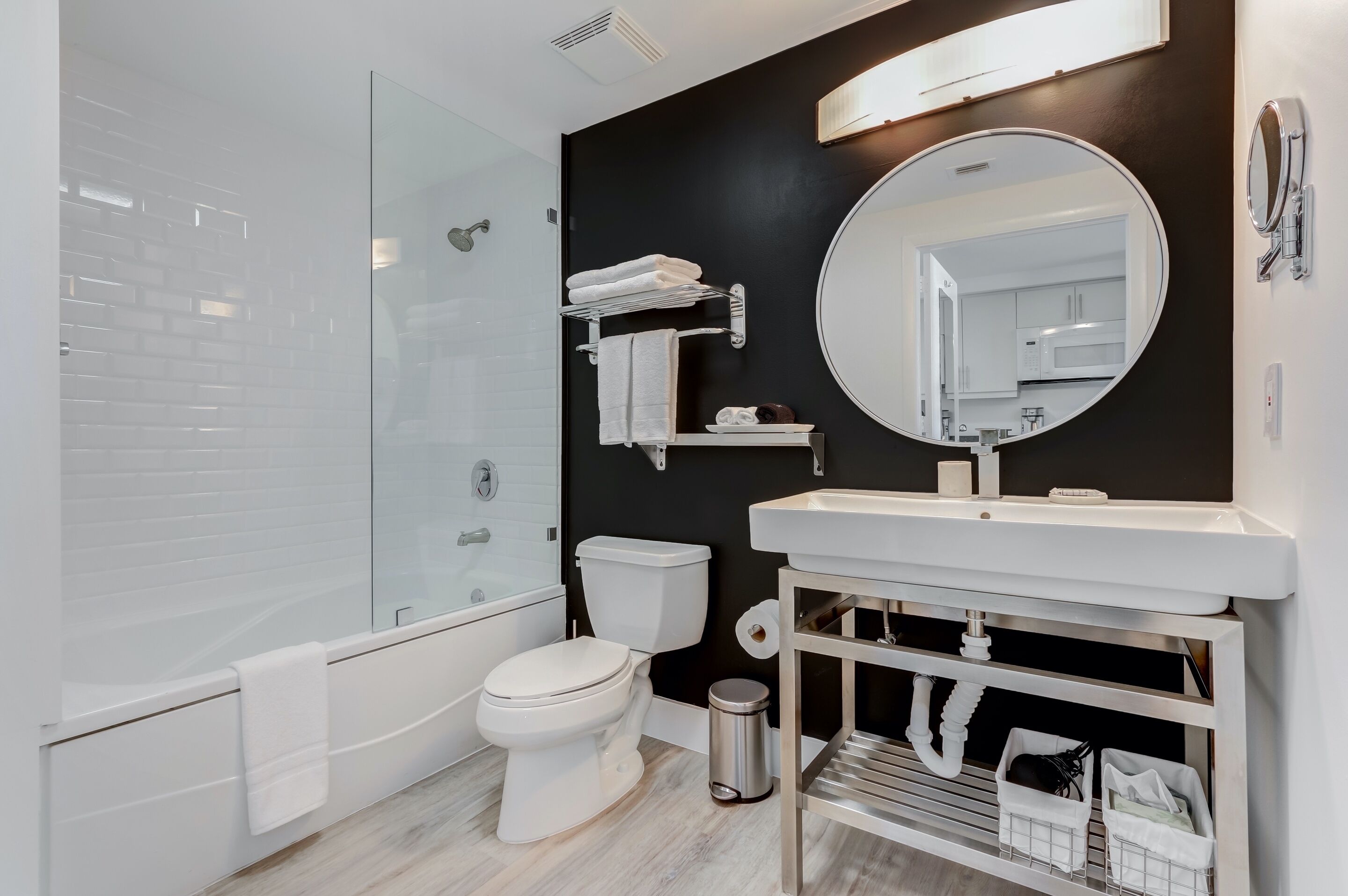 Un bagno moderno con cabina doccia in vetro, un water bianco, una vasca da bagno, un lavabo con specchio e una parete d'accento nera.