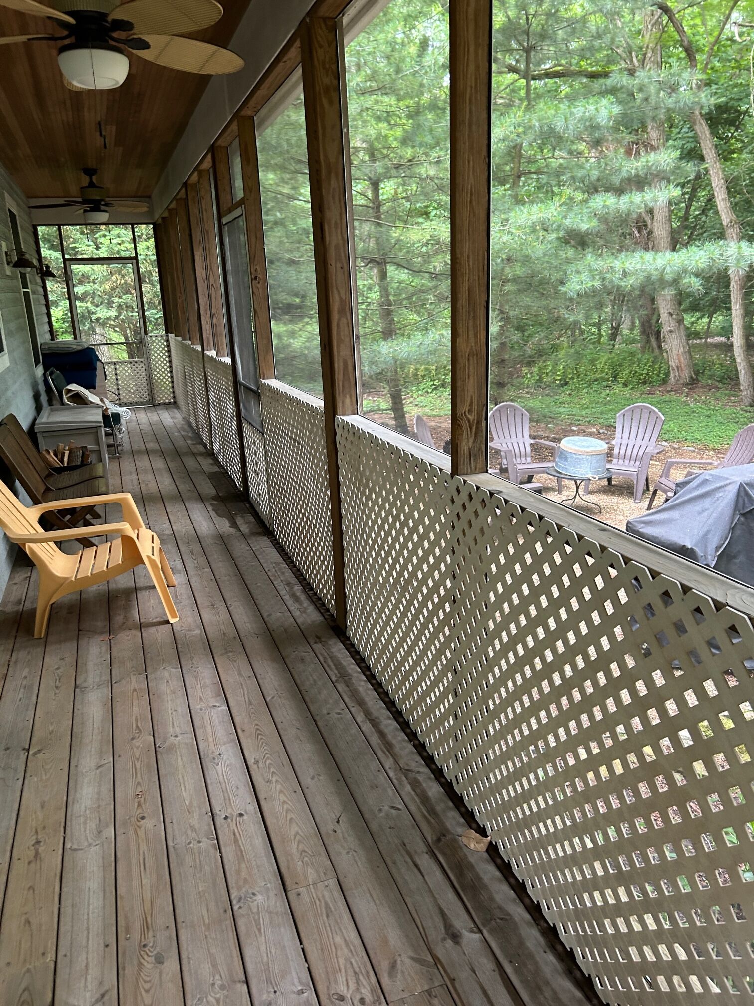 A covered porch with wooden flooring, a ceiling fan, and a view of a forest.