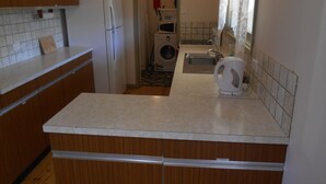 Une cuisine de taille réduite, dotée de meubles en bois, d’un réfrigérateur blanc, d’un lave-linge et d’un évier.
