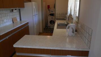 A compact kitchen with wooden cabinets, a white refrigerator, a washing machine, and a sink.