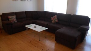 Un salon avec un canapé d’angle, une petite table blanche et un plancher en bois.