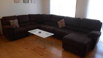 A living room with a sectional sofa, a small white table, and wooden flooring.