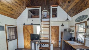 A rustic kitchen with wooden beams, a lofted sleeping area, a ladder, and a welcome sign. - Black Hills Farmhouse, Cabin #3 (Custer)