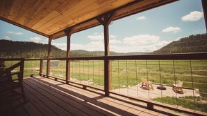 A wooden deck with a view of a grassy field and mountains. - Black Hills Farmhouse, Cabin #3 (Custer)