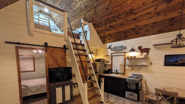 A rustic cabin interior with a loft bedroom, a kitchen with a stove, and a dining area. - Black Hills Farmhouse, Cabin #3 (Custer)