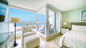 Una habitación de hotel con un balcón grande, una cama, una silla y una mesita de noche.