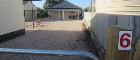A fenced property with a sandy driveway leading to a building with a dark roof.