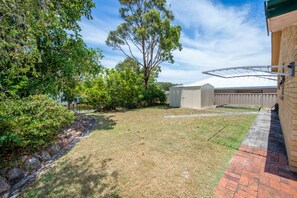 A backyard with a lawn, a shed, and a tree. - Government Road Shoal Bay Family Holiday Home (Shoal Bay)