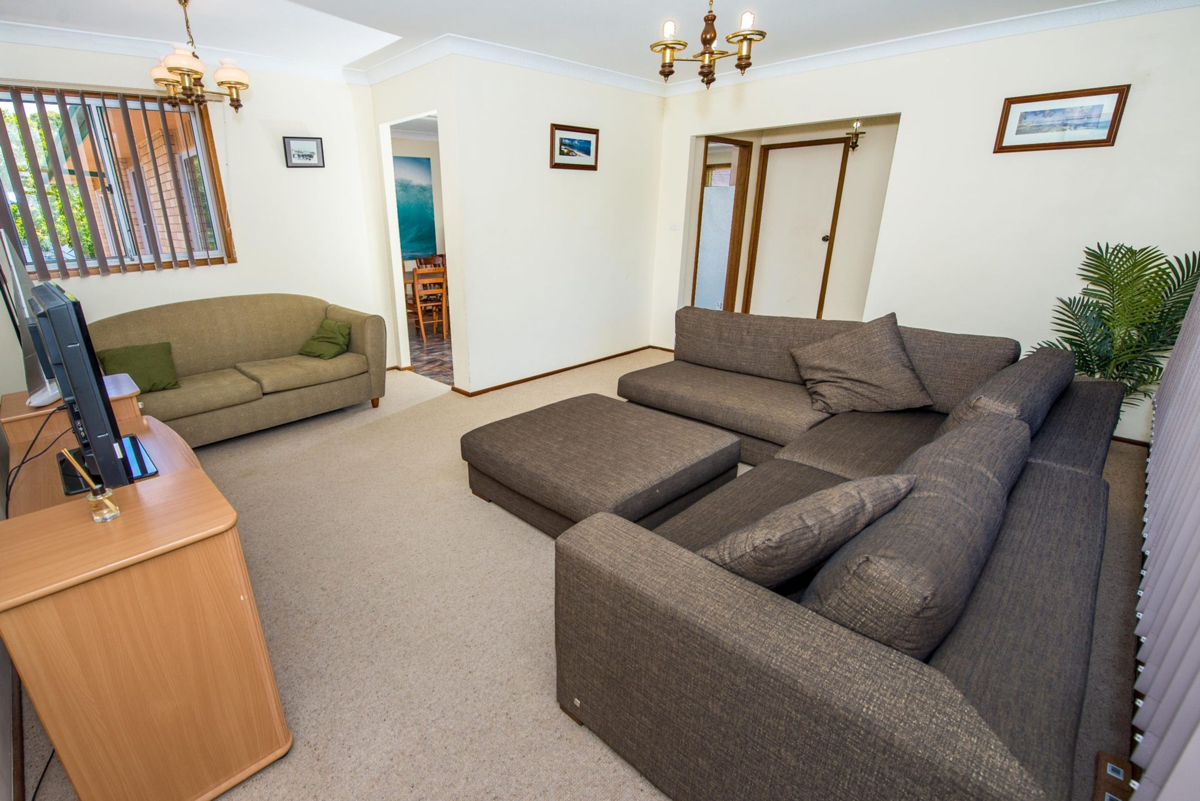 A living room with a sectional sofa, a television on a wooden stand, and a door leading to another room.