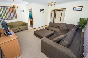 Ein Wohnzimmer mit einer Eckcouch, einem Fernseher auf einem Holzboden und einer Tür zu einem weiteren Raum.