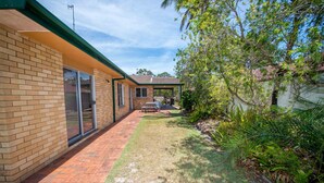 A residential property with a brick exterior, a covered patio area, and a well-maintained lawn. - Government Road Shoal Bay Family Holiday Home (Shoal Bay)