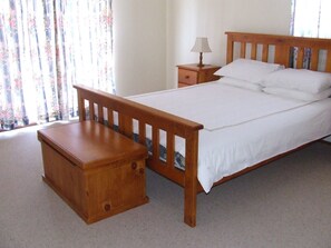 A bedroom with a wooden bed, a bedside table, a nightstand, and a lamp. - Government Rd 63 - Shoal Bay (Shoal Bay)