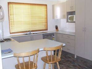 A compact kitchen with a central island, two wooden chairs, a built-in oven, and a microwave. - Government Road Shoal Bay Family Holiday Home (Shoal Bay)