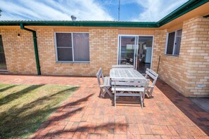 A patio with a wooden table and chairs, a brick wall, and a sliding glass door leading to an indoor area. - Government Rd 63 - Shoal Bay (Shoal Bay)