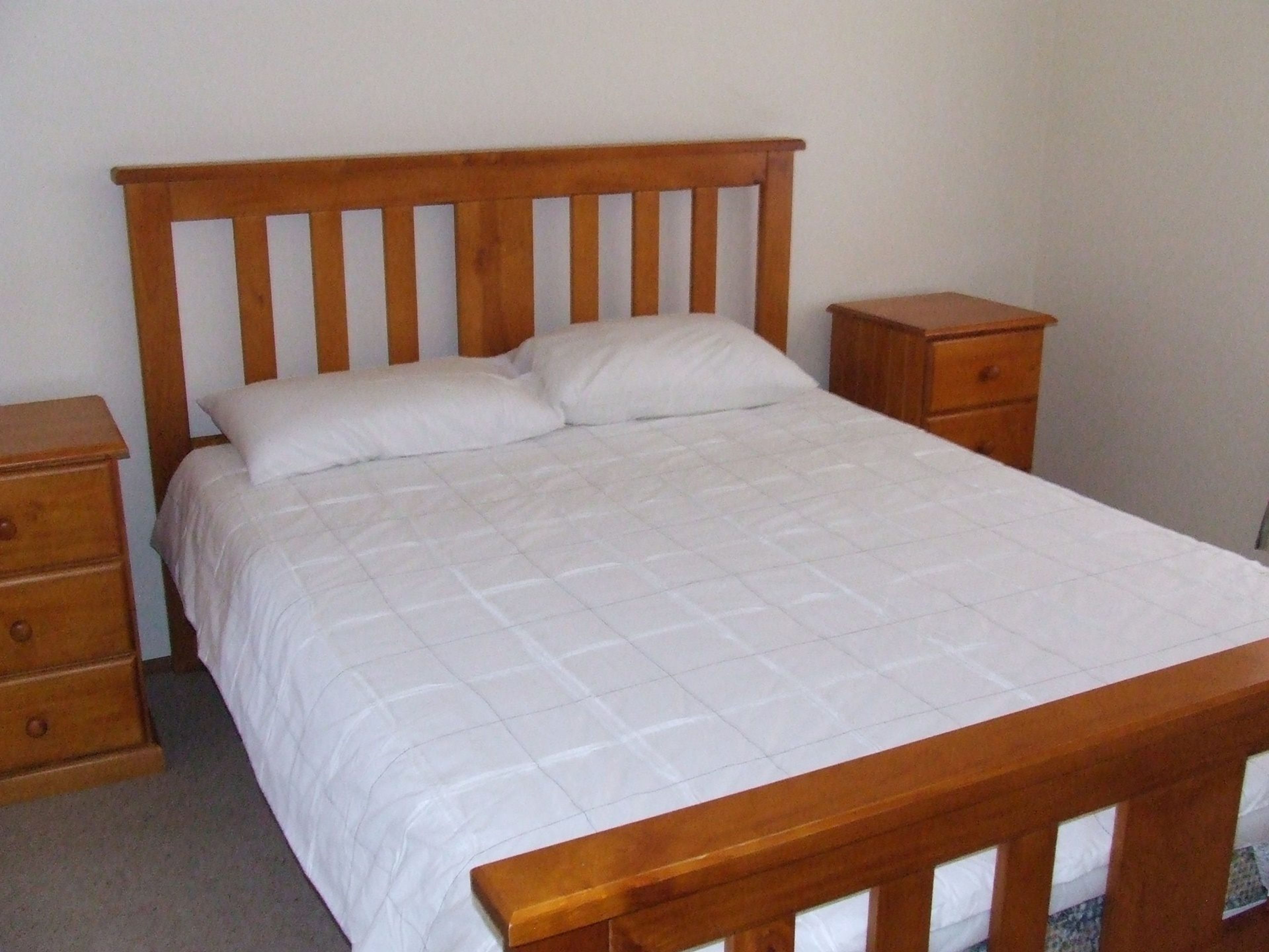A single bed with a wooden headboard, two bedside tables, and a wooden nightstand.
