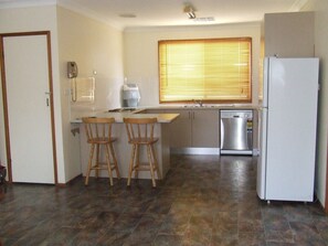 A compact kitchen with a built-in dishwasher, a refrigerator, and a window with blinds.