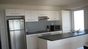 A modern kitchen with white cabinets, a stainless steel refrigerator, a microwave, and a large island with a sink.