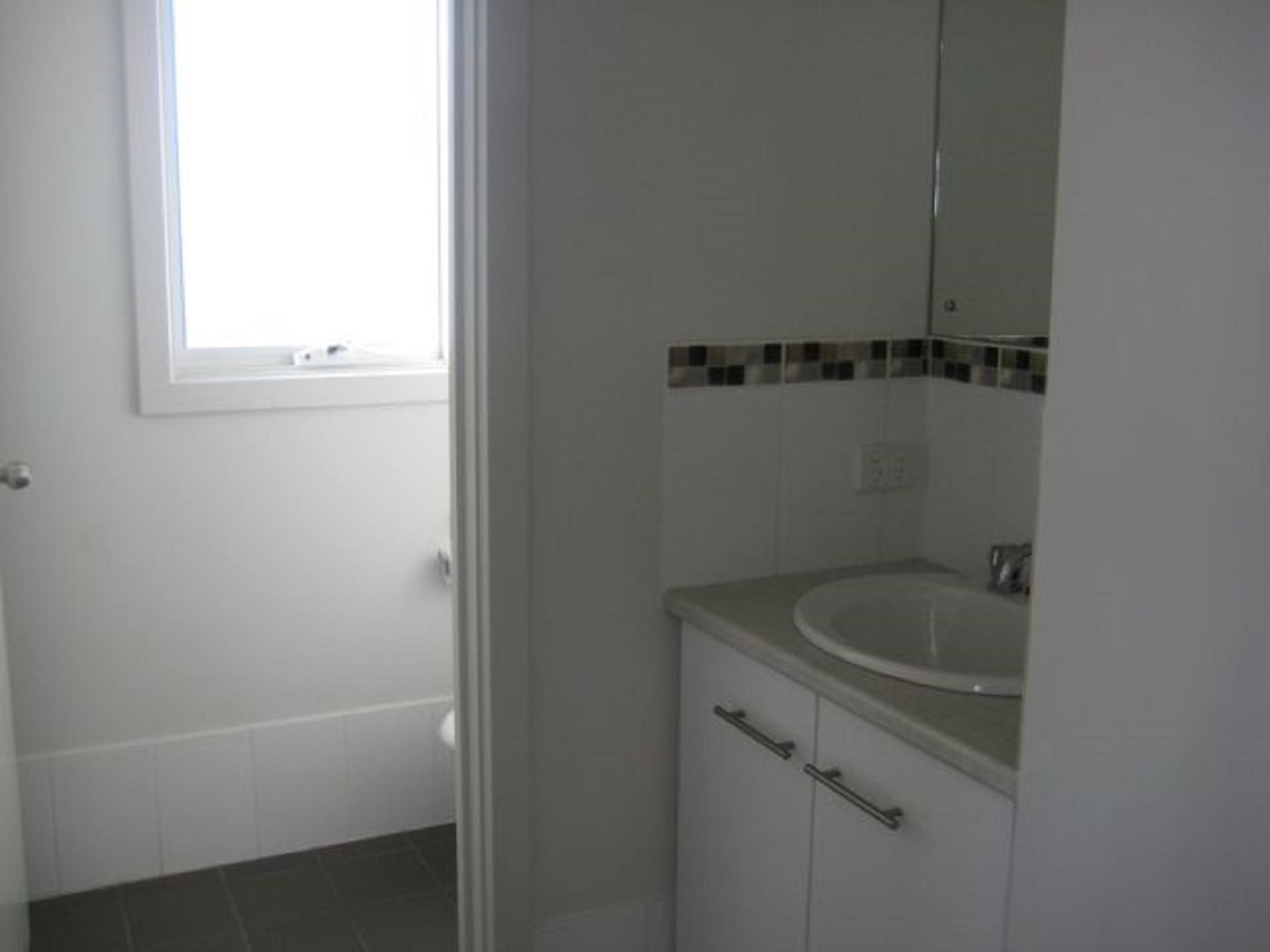 Une salle de bain avec un lavabo blanc, un miroir et une fenêtre.