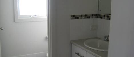 Une salle de bain avec un lavabo blanc, un miroir et une fenêtre.