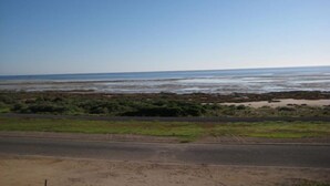 A coastal road with a sandy beach and sparse vegetation.