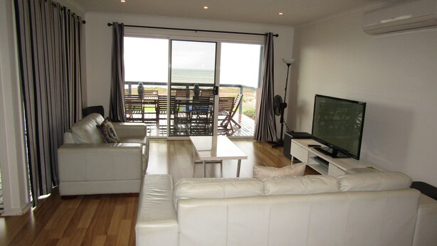 A modern living room with a white sofa, a TV, and a view of the outdoors.