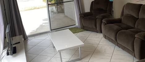 A living room with a white coffee table, two brown sofas, a TV, and a sliding glass door leading to a patio.