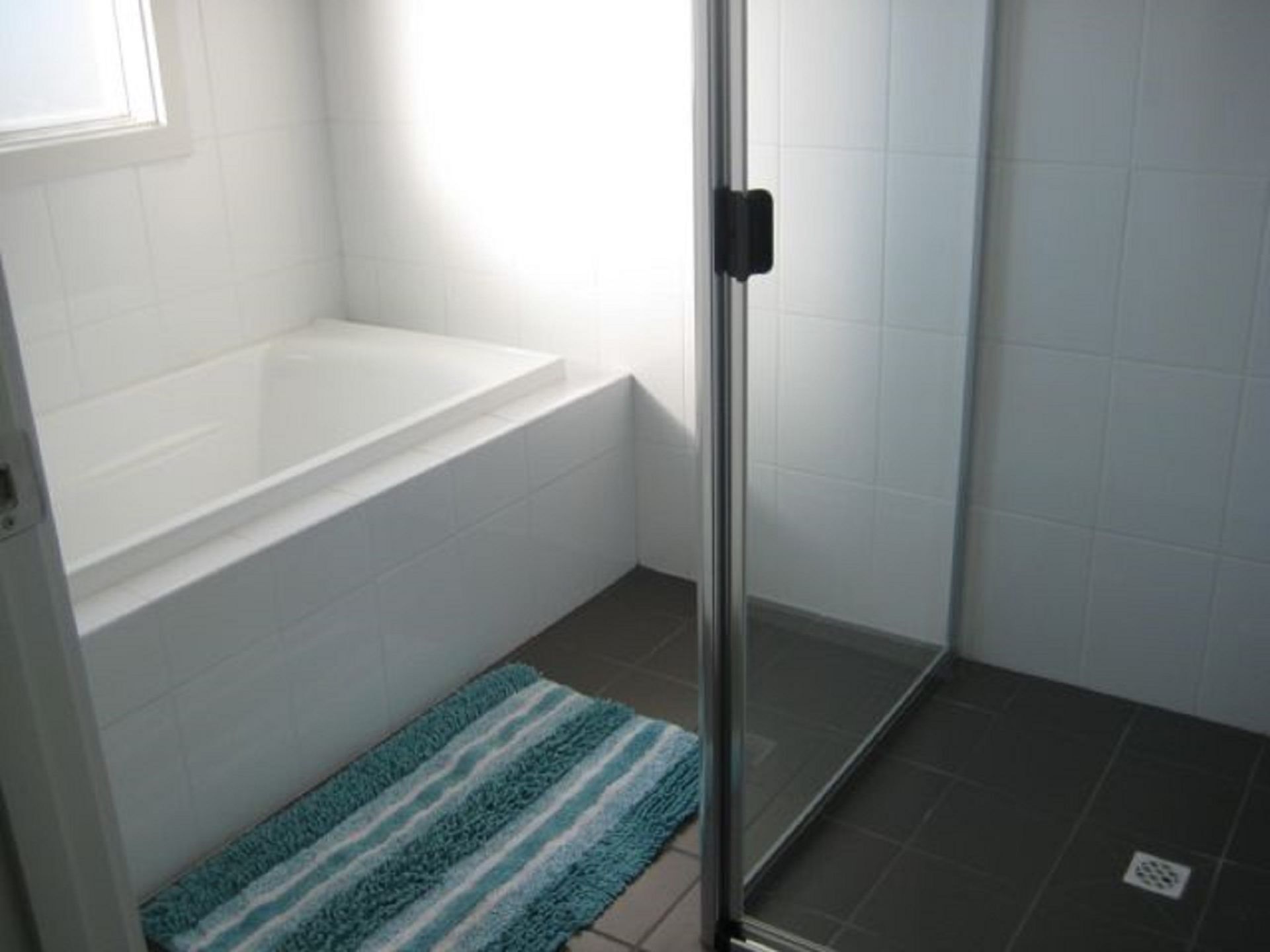 A bathroom with a bathtub, a shower area, and a blue striped rug.