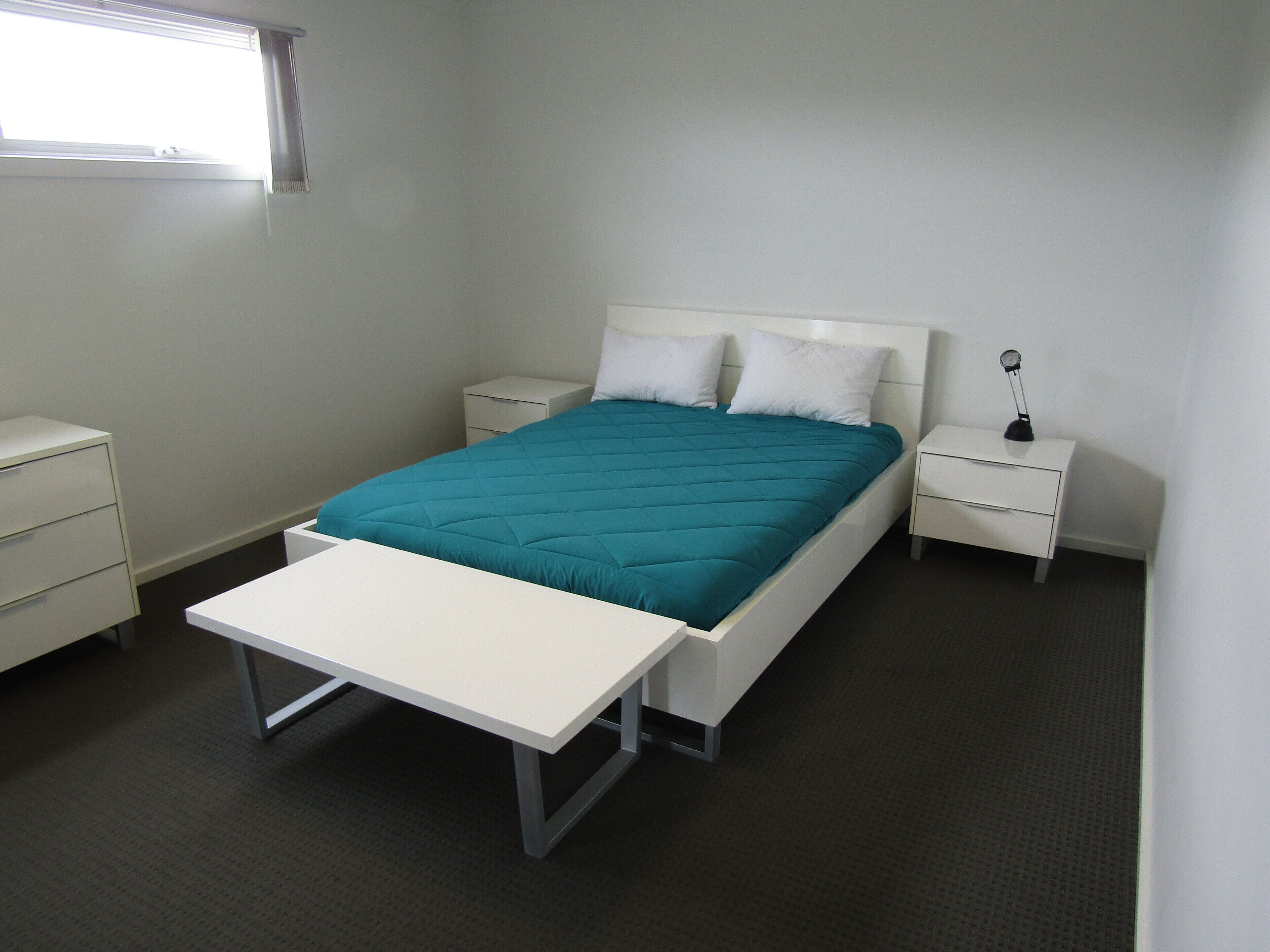 Ein ordentlich eingerichtetes Schlafzimmer mit Bett, Nachttischen und Schreibtisch.
