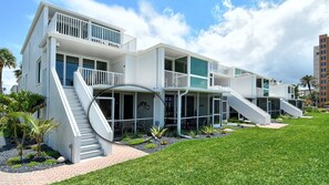 A modern multi-story building with balconies, a central staircase, and a well-maintained lawn.