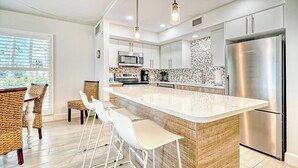 A modern kitchen with a central island, stainless steel appliances, and a view to the outside. - LaPlaya 101A - Step out to the beach.  Light and bright end unit. (Longboat Key)