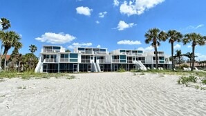 A beachfront property with multiple balconies, a sandy beach in the foreground, and palm trees. - LaPlaya 101A - Step out to the beach.  Light and bright end unit. (Longboat Key)