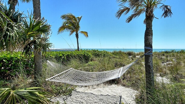 A hammock tied between trees on a sandy beach with palm trees and a clear blue sky in the background. - LaPlaya 101A - Step out to the beach.  Light and bright end unit. (Longboat Key)