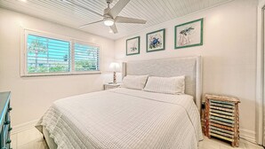 A bedroom with a bed, a ceiling fan, a nightstand, a lamp, and framed artwork on the wall. - LaPlaya 102E-Tropical garden view near the pool! (Longboat Key)