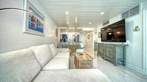 A modern living room with a sofa, a coffee table, and a kitchen area with a fridge and stove.